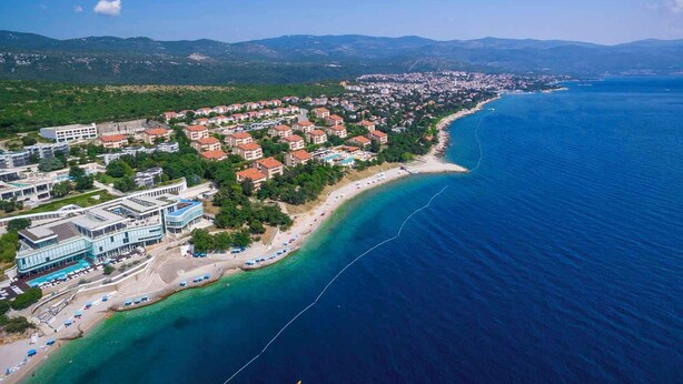 Vue aérienne d’une ville côtière avec une plage, des immeubles résidentiels et une mer bleue et limpide.