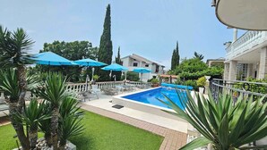 Une piscine bordée de parasols bleus, entourée de palmiers et d’une pelouse bien entretenue.