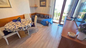 Une pièce comprenant une table à manger, un canapé, un balcon avec vue et une fenêtre.