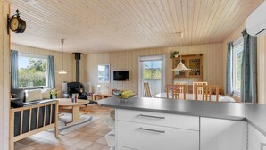 Una cucina moderna con soffitto in legno, zona pranzo con tavolo e sedie, e piano cottura integrato.