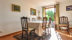Un coin repas avec une table dressée pour quatre personnes, entourée de chaises en bois, d’un tapis à motifs et de deux tableaux accrochés aux murs.