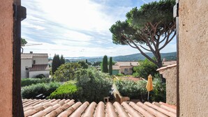 Une cour avec des tuiles en terre cuite sur le toit, un parasol jaune et une vue sur les bâtiments et les collines environnants.