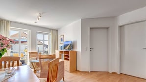 Un salon moderne comprenant un coin repas, des meubles en bois, un téléviseur à écran plat et une vue sur l’extérieur.