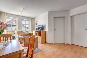 A modern living room with a dining area, wooden furniture, a flat-screen TV, and a view of the outside.