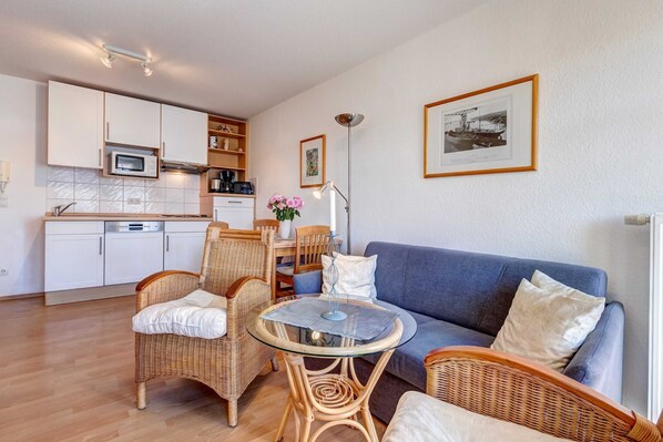 A compact living space with a kitchenette, a dining area, and a seating area with a blue sofa and wicker chairs.