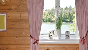L’intérieur d’une cabane avec un mur en bois, une fenêtre donnant sur un lac et deux décorations en forme de cœur posées sur le rebord de la fenêtre.