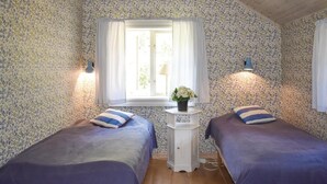 Une chambre avec deux lits, un papier peint à motifs floraux, une fenêtre avec des rideaux, une petite table avec un vase et des lampes de chevet.
