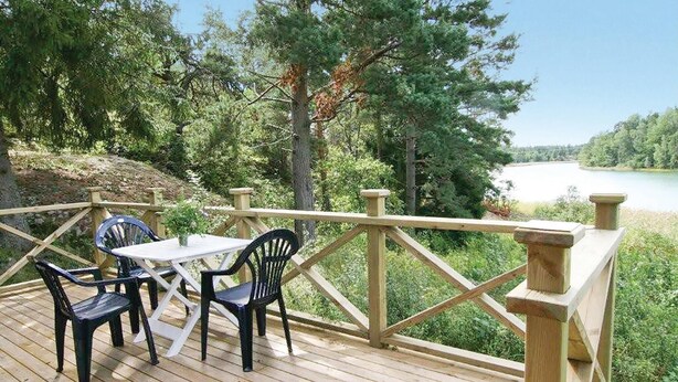 Une terrasse en bois avec une table et deux chaises, donnant sur un lac et entourée d’arbres.