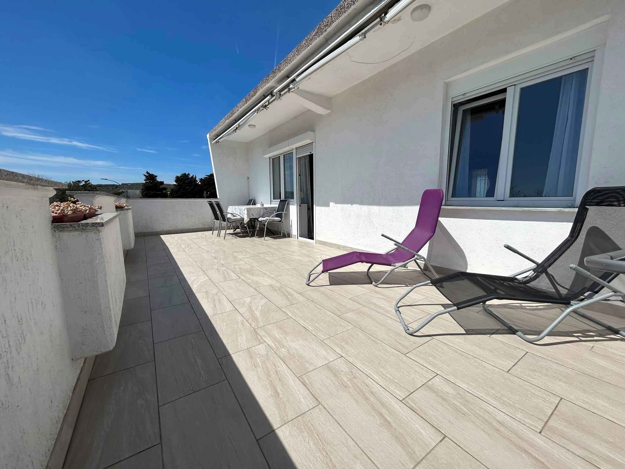 A rooftop terrace with a table and chairs, a purple lounge chair, and a view of the surrounding landscape.