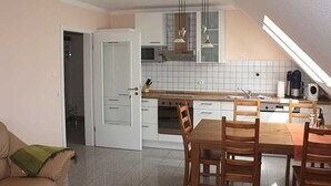 A compact kitchen with white cabinets, a dining table with chairs, and a ceiling fan.