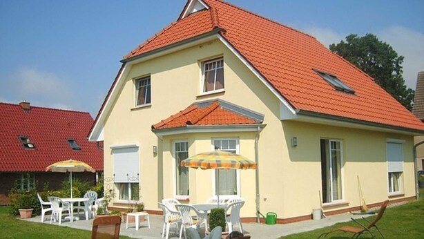 A two-story house with a red-tiled roof, a covered patio with outdoor furniture, and a lawn.