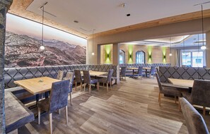 Un restaurant avec des poutres en bois au plafond, des sièges rembourrés et une fresque représentant un paysage de montagne.