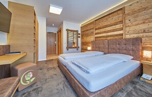 Une chambre d’hôtel avec un panneau mural en bois, un lit avec une literie blanche, un bureau avec une chaise et une petite table de chevet avec une lampe.