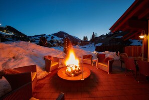 Un pozo de fuego con sillas, nieve y una montaña al fondo.