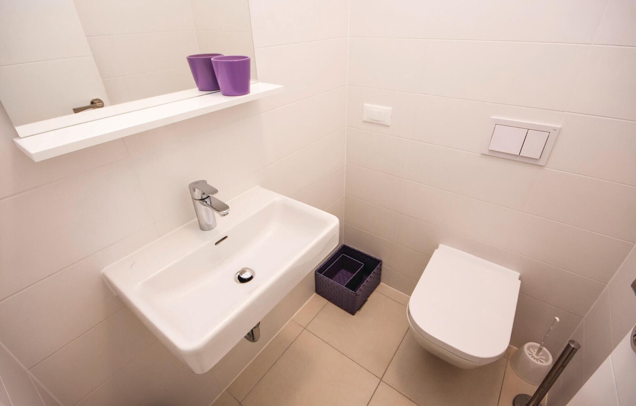 Un bany amb un lavabo blanc, un vàter i una cistella morada a terra.