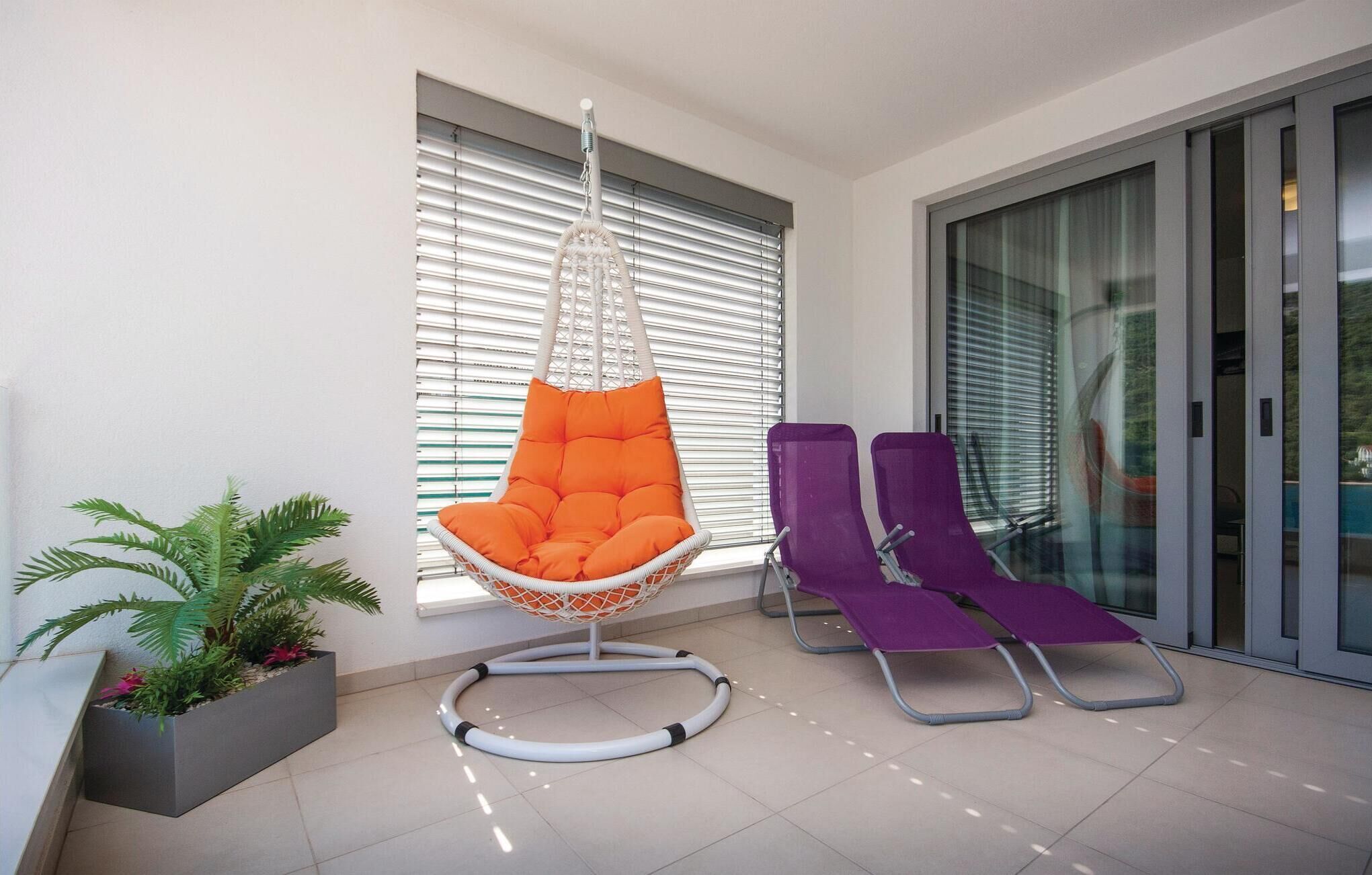 A modern outdoor seating area with a hanging orange chair, a purple lounge chair, and a potted plant.