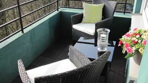 Un balcone con mobili in vimini, un tavolo in vetro e un addobbo floreale.
