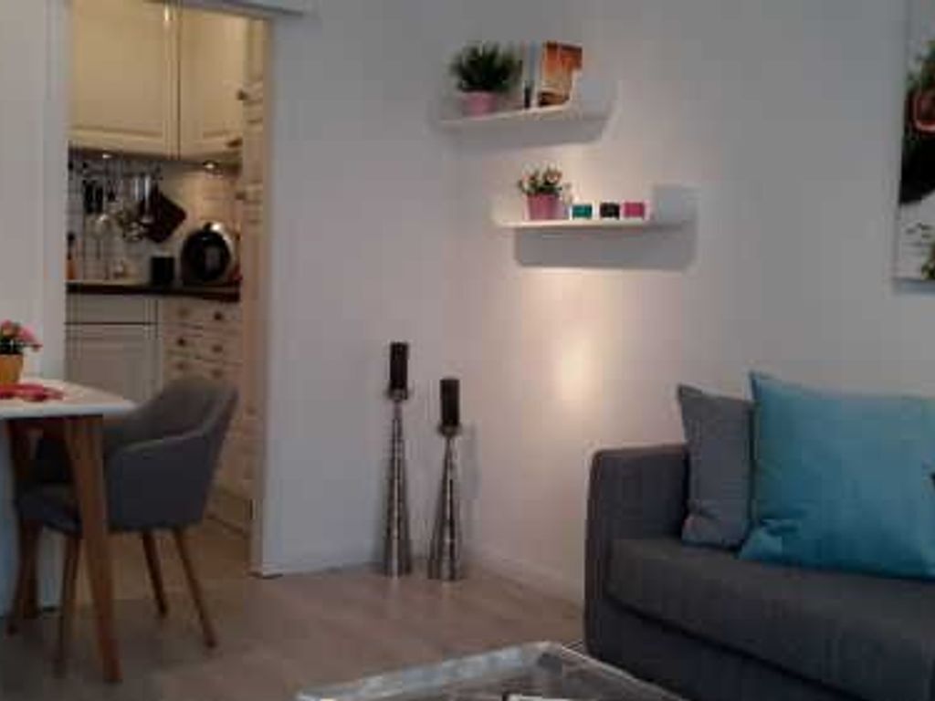 En moderne stue med en grå sofa, et spisebord med stole, og et køkken, der ses gennem en åben dør.