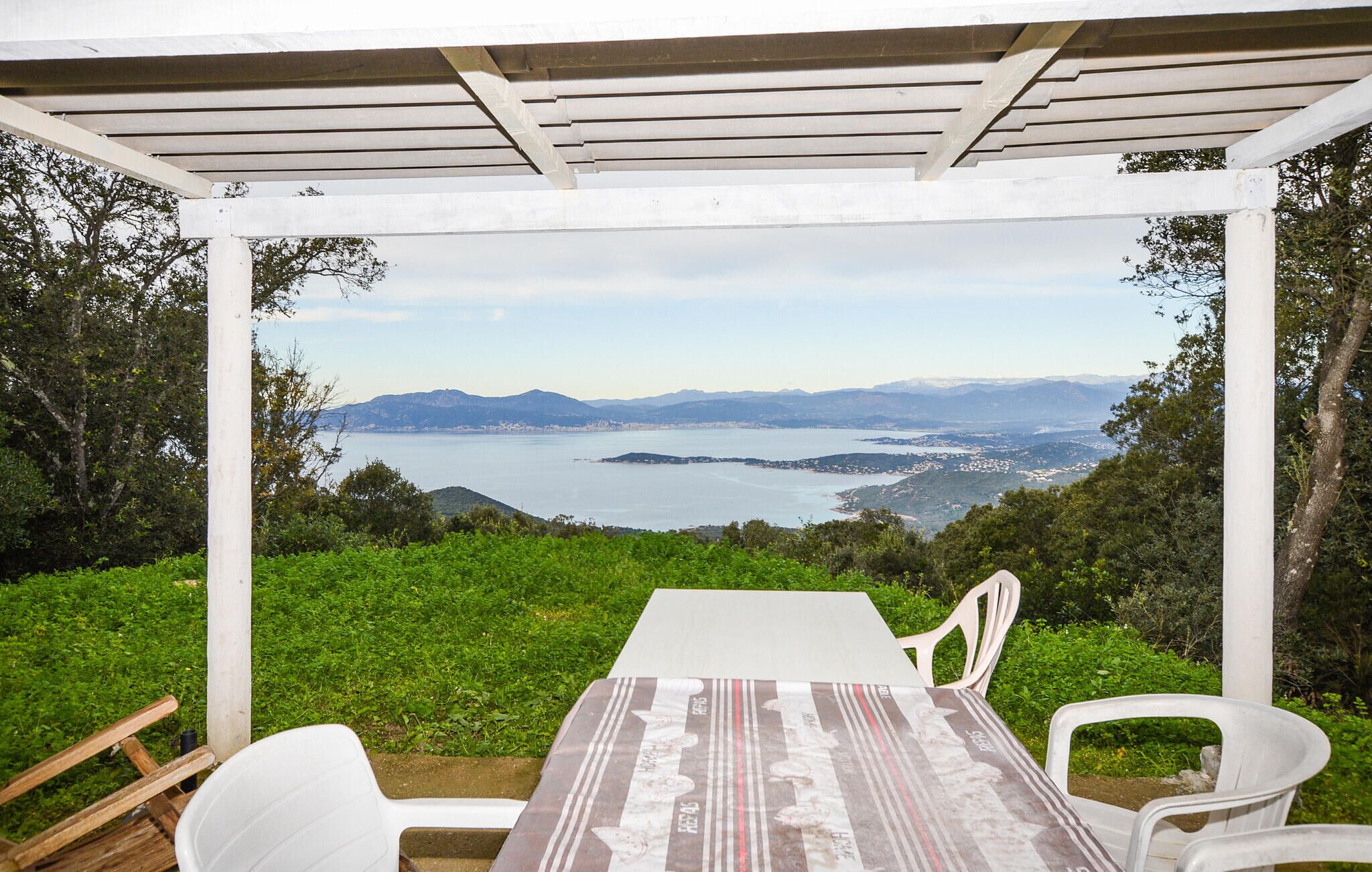 A covered outdoor seating area with a table and chairs, overlooking a scenic view of a lake and distant mountains.