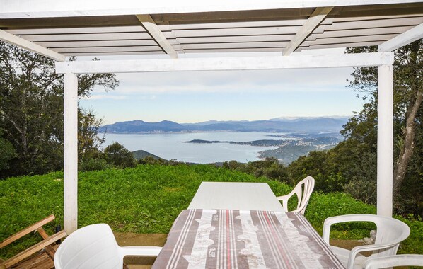 Un espace extérieur abrité, doté d’une table et de chaises, offrant une vue panoramique sur un lac et des montagnes lointaines.