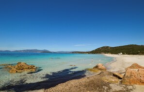 Une plage bordée d’une eau turquoise et limpide, d’un rivage rocheux et d’un paysage vallonné en arrière-plan.