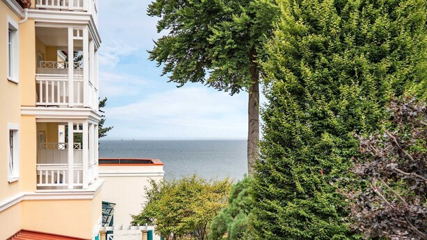 A coastal building with balconies overlooking the sea, surrounded by lush greenery.