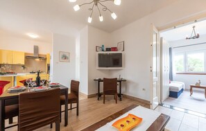 Une cuisine moderne avec un coin repas, un téléviseur à écran plat et une vue sur la chambre à coucher par une porte ouverte.
