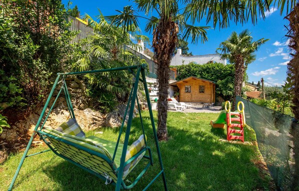 Enjoy a family-friendly outdoor space with a swing set and playhouse amidst lush greenery and palm trees.