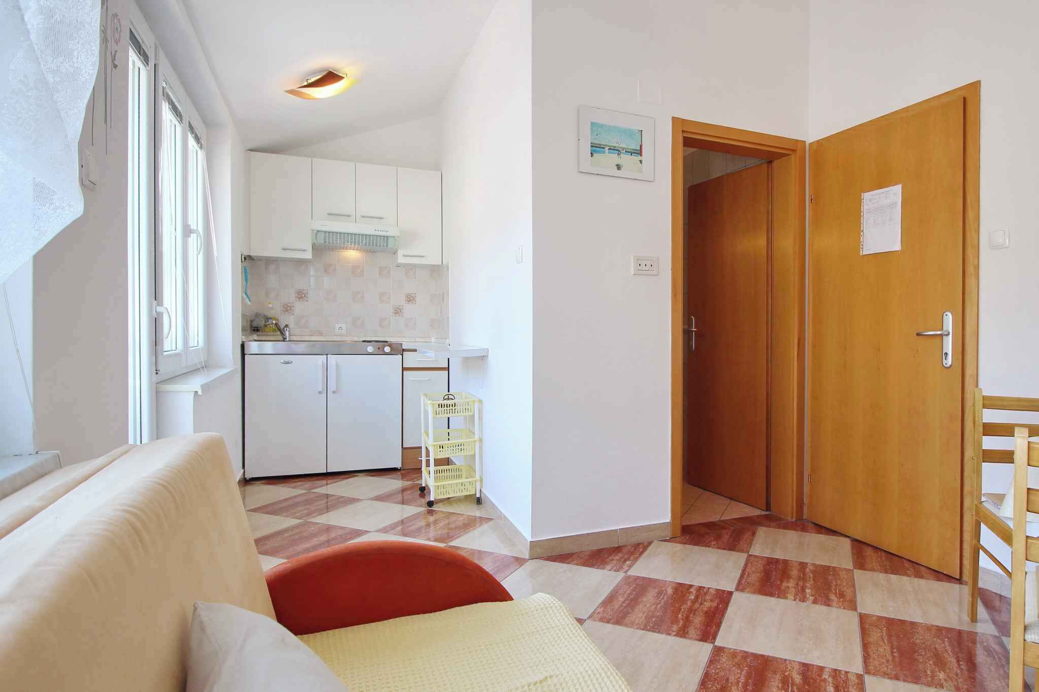 Un espacio habitable compacto con kitchenette, una puerta de madera y piso a cuadros.