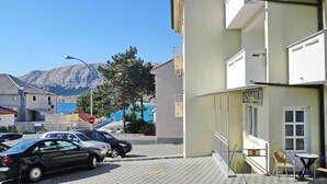 Un bâtiment avec une enseigne indiquant « AVARLI » au rez-de-chaussée, un parking avec des voitures et une montagne en arrière-plan.