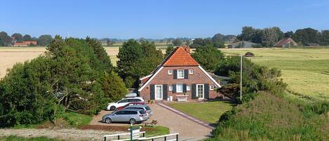 A traditional brick house with a red roof, surrounded by a grassy field and trees.