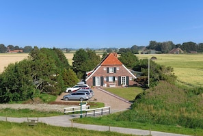 A traditional brick house with a red roof, surrounded by a grassy field and trees.