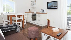 Eine moderne Küche mit weißen Schränken, einer Holzarbeitsplatte und einem eingebauten Backofen. Es gibt einen Essbereich mit einem weißen Tisch und Stühlen, sowie ein großes Fenster, das für natürliches Licht sorgt.