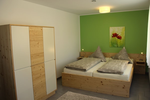 A bedroom with a wooden bed, a wardrobe, and a green wall with a flower painting.