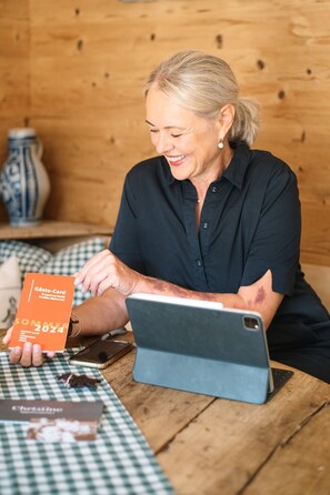 Uma pessoa sentada a uma mesa de madeira com um laptop, segurando um cartão com a inscrição 'Gästecard Sommer 2024'.