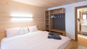 Ein modernes Schlafzimmer mit einem Holz-Kopfteil, einem Bett mit weißen Leinen, einem Einbauschrank mit Kleiderstange und einem Nachttisch mit einer Zeitschrift.