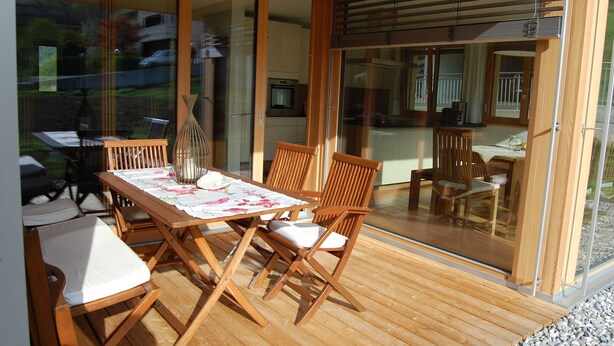 Eine Holzdar Terrasse mit Tisch und Stühlen, eine Glastür, die zur Küche führt, und ein Blick ins Freie.