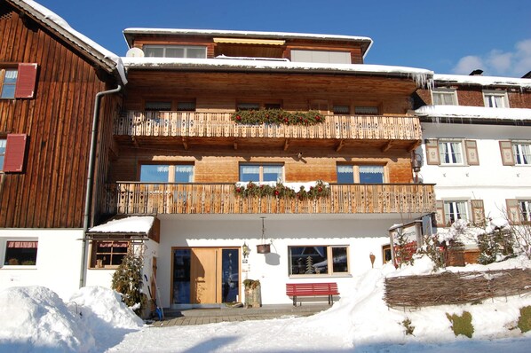 A multi-story wooden building with balconies, a wooden fence, and a bench.
