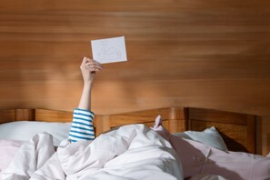 A person lying in bed with a drawing of a person in a dress, holding a card.