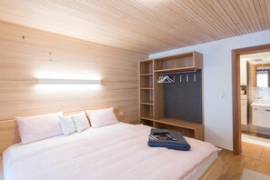 Un dormitorio moderno con cabecera de madera, cama con ropa de cama blanca, armario empotrado con espacio para colgar y mesita de noche con una revista.