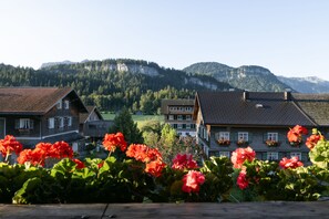 A residential area with traditional houses, a mountain backdrop, and vibrant red flowers in the foreground.