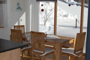 A wooden dining table with four chairs, a floral tablecloth, and a view of a snow-covered landscape through a window.