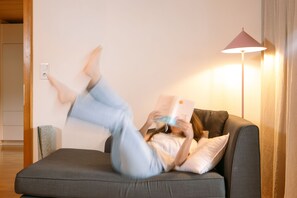 A person lying on a sofa with a book, a lamp, and a power outlet in the room.