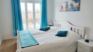 Quarto com duas camas, janela com cortinas, mesa de cabeceira com abajur e um quadro na parede.