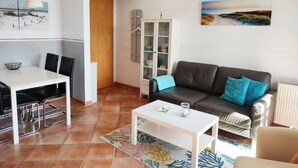 Uma sala de estar com um sofá marrom, uma mesa de centro branca e uma área de jantar com uma mesa e cadeiras brancas.