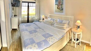 A bedroom with a large bed, a nightstand, a lamp, and a painting of a beach scene.