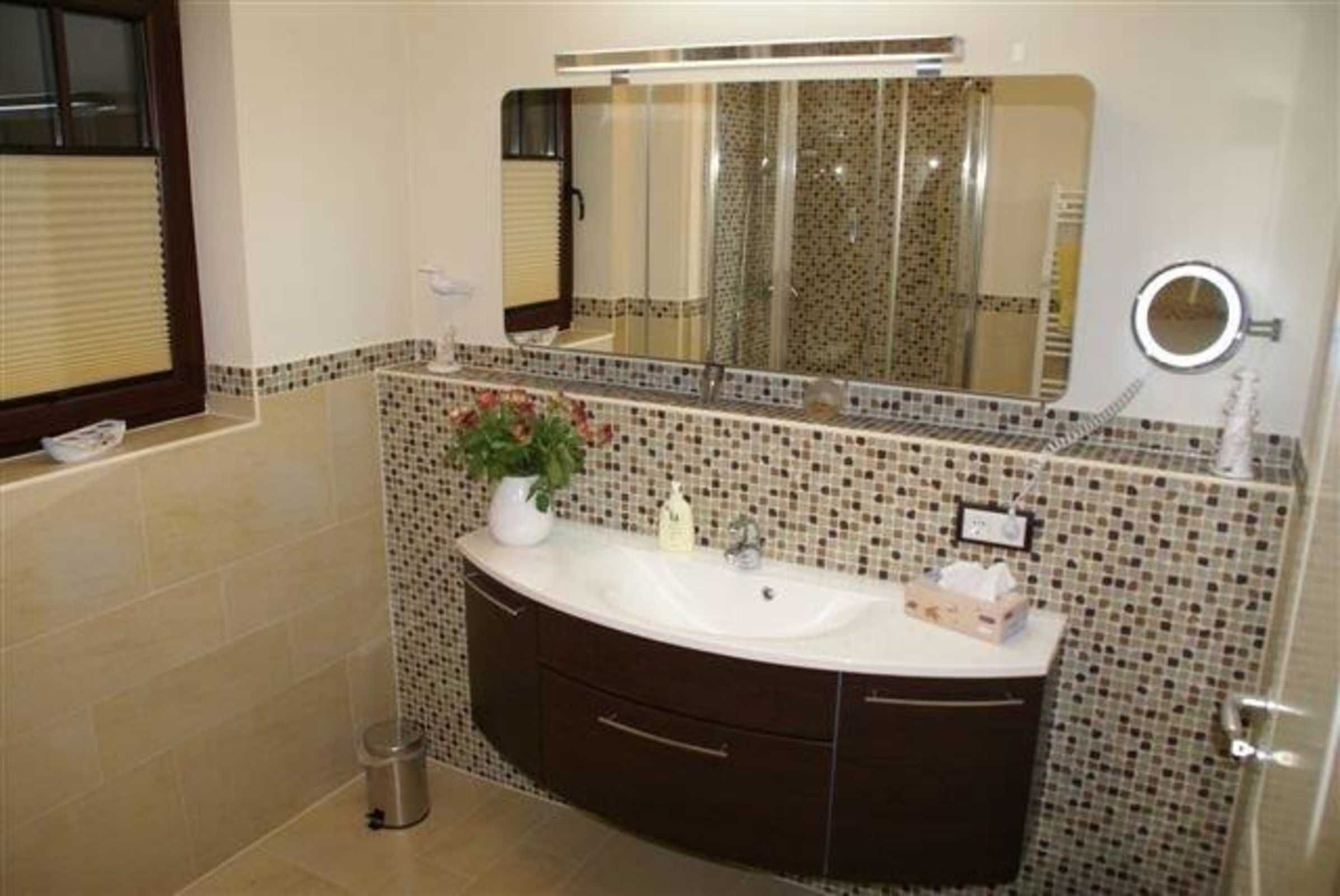 A bathroom with a white sink, dark cabinets, a mirror, and a tiled backsplash.
