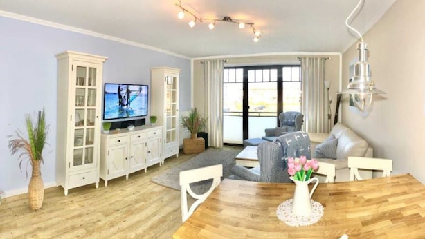A living room with a wooden dining table, white cabinets, a television, and a large window with curtains.
