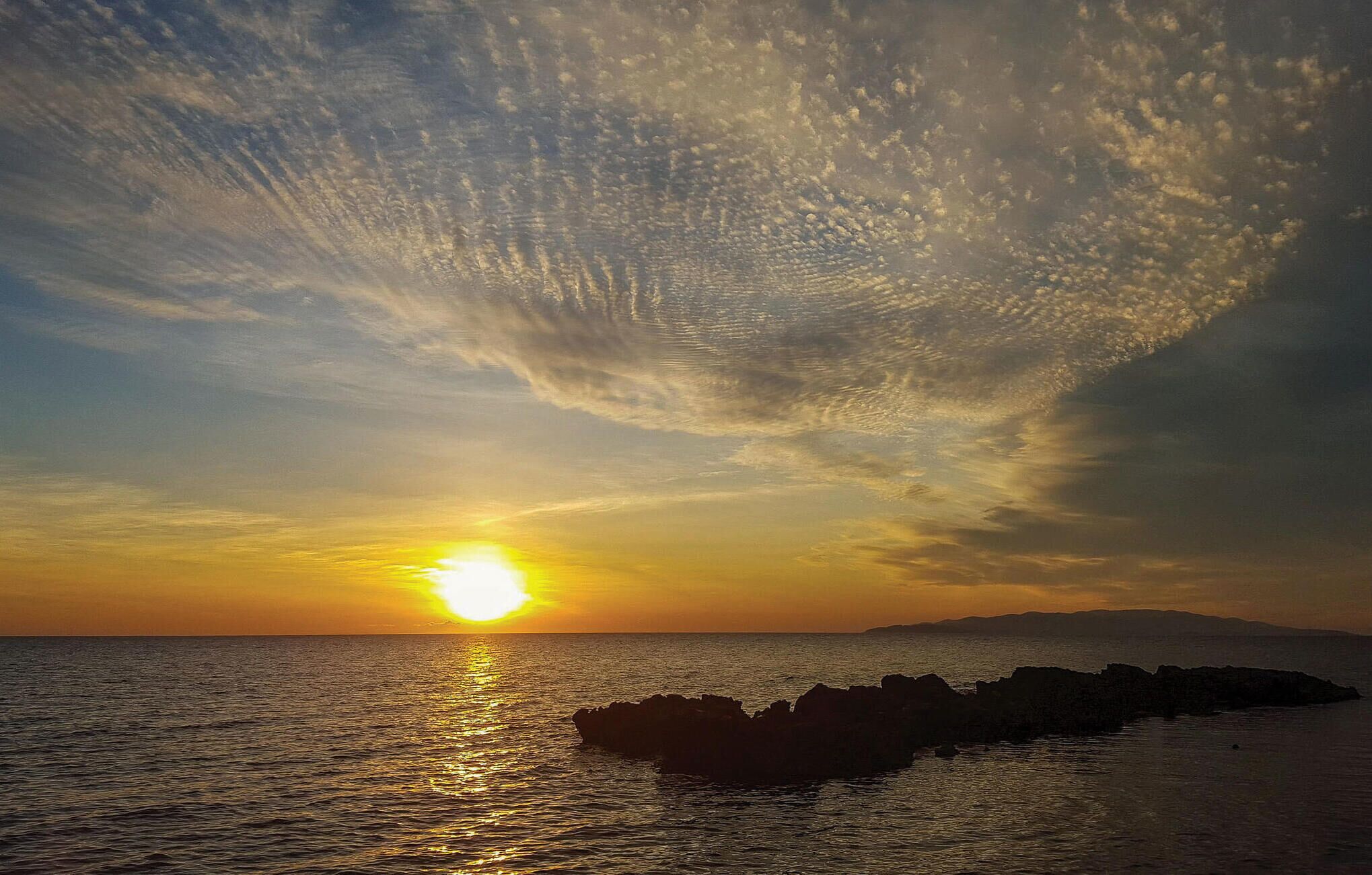 A sunset over the ocean with a rocky shoreline.