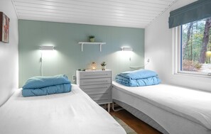 A bedroom with two beds, a dresser, a shelf with a plant, and a window with a forest view.